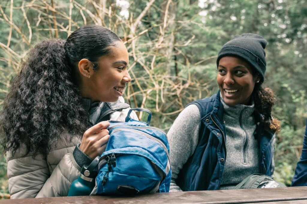 Two women enjoying a hiking break, smiling and chatting at a picnic table.